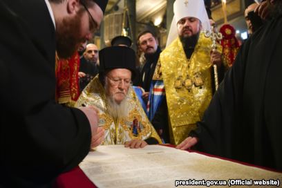 Вселенський патріарх Варфоломій підписує томос про автокефалію для Православної церкви України (ПЦУ). По ліву руку від нього стоїть митрополит Київський і всієї України Епіфаній. Стамбул, 5 січня 2019 року