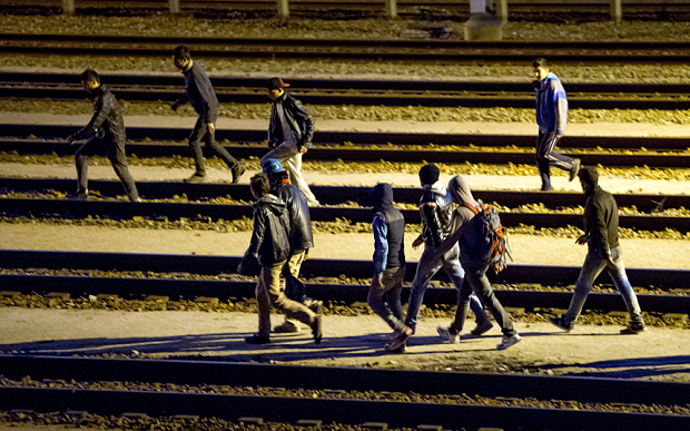 Подпись под фото: Мигранты идут по железнодорожным путям евротуннеля на границе в Кале